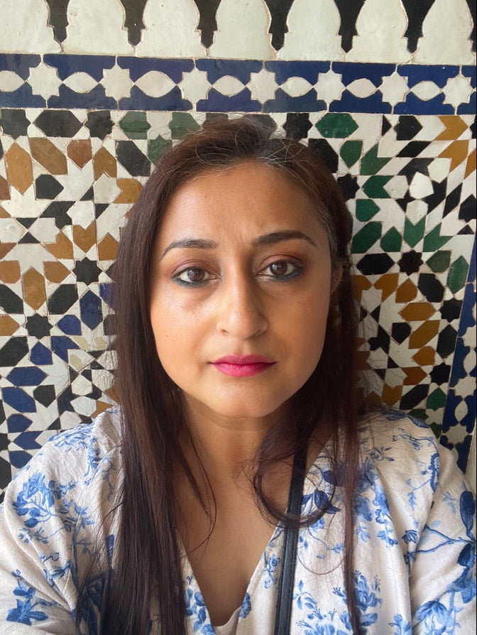 Woman with long dark hair wearing a floral blouse against a patterned wall.